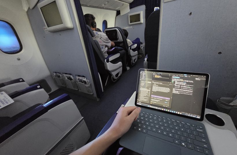 Bill coding on a laptop mid-flight on an airplane, window visible